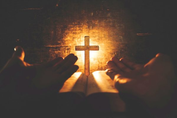 conceptual image focus on candle light with man hand holding wooden cross on bible and blurred world globe in the dark room, christian symbol show Jesus is the light of the world