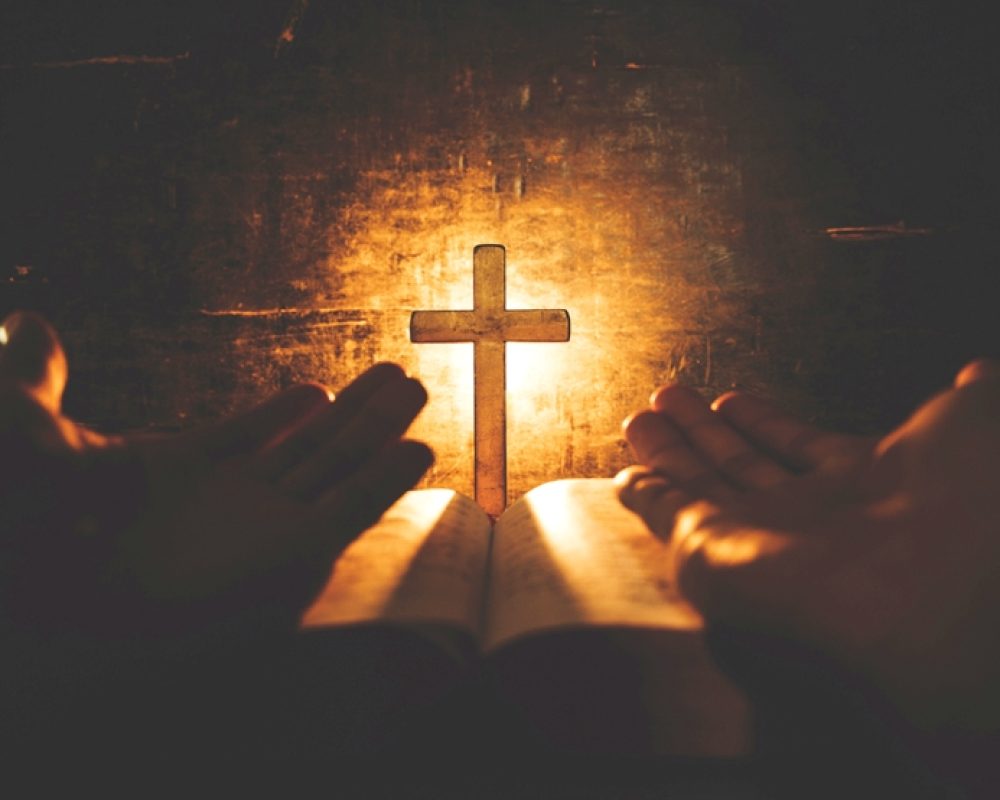 conceptual image focus on candle light with man hand holding wooden cross on bible and blurred world globe in the dark room, christian symbol show Jesus is the light of the world